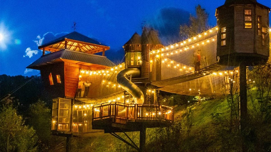People playing on the bridges and in the trees houses adorned with yellow lights at night at Anakeesta in Gatlinburg, Tennessee, USA