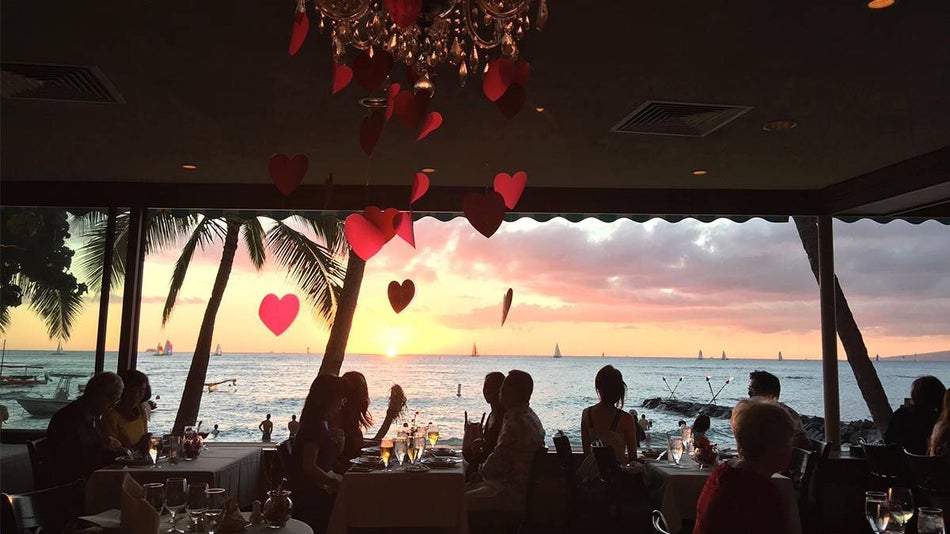 An open air dining room filled with people dining and a chandelier with paper hearts falling from it at Michel’s at the Colony Surf in Honolulu, Hawaii, USA