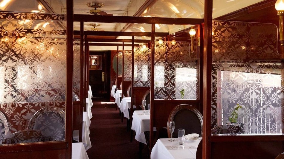 Interior view of white table cloth covered dining areas sections off with scetched glass on the Napa Valley Wine Train