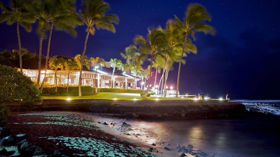 night shot of The Beach House Kauai exterior surrouned by palm trees and glowing lights on the beach