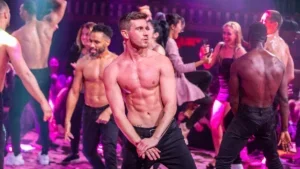 Close up of a fit shirtless man with black pants with other fit shirtless men behind them and a couple of women on a stage with purple lighting at Magic Mike Live in Las Vegas, Nevada, USA