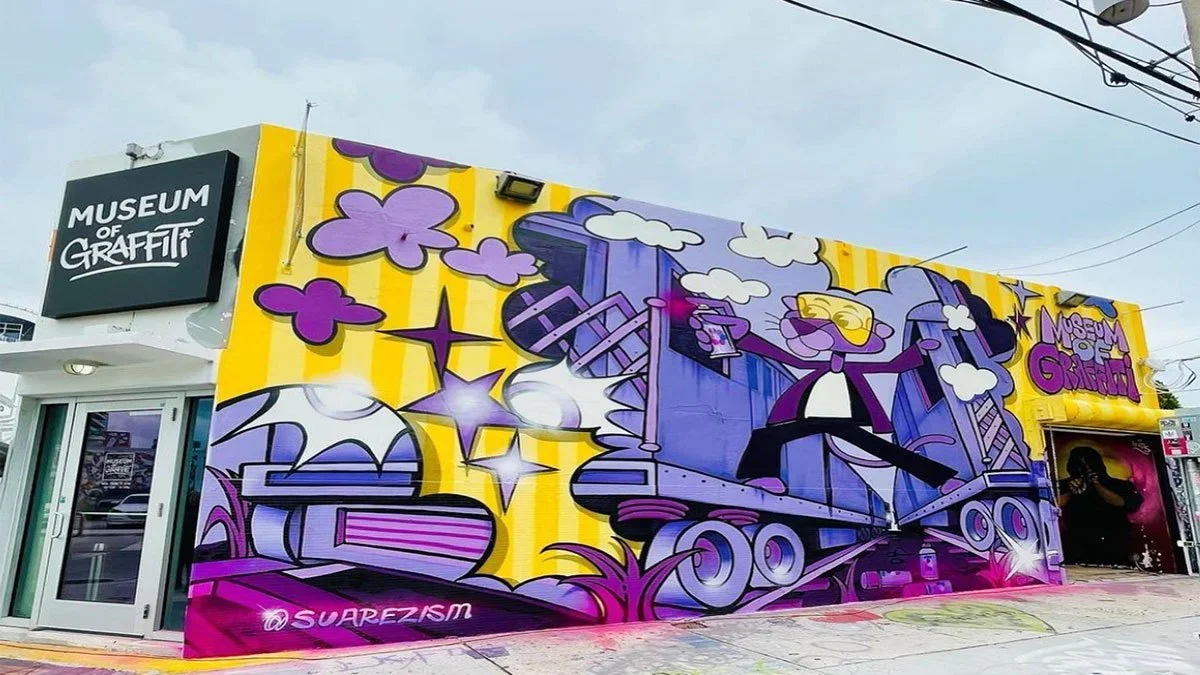 Large wall of yellow and purple graffiti depicting a panther spray painting on the side of the Museum of Graffiti in Miami, Florida
