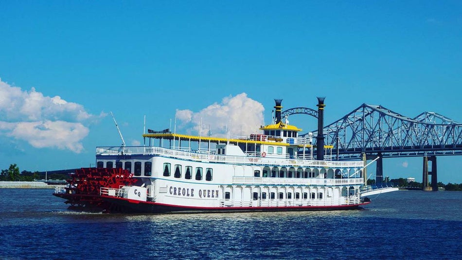 Large cruise boat named Creole Queen on the water with a bridge and a bright blue sky behind it in New Orleans, Louisiana