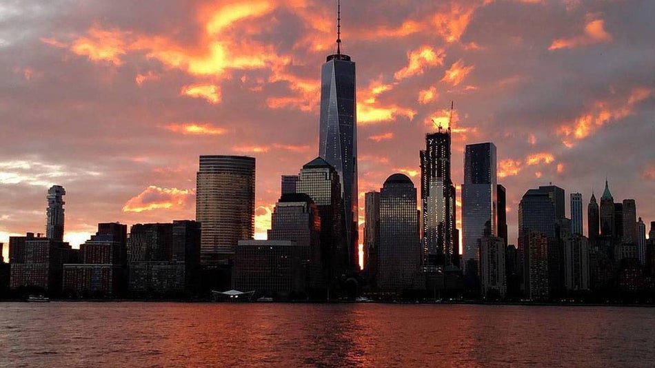 View looking at the One World Observatory from the water with a light pink and orange sunset behind it in NYC, New York, USA
