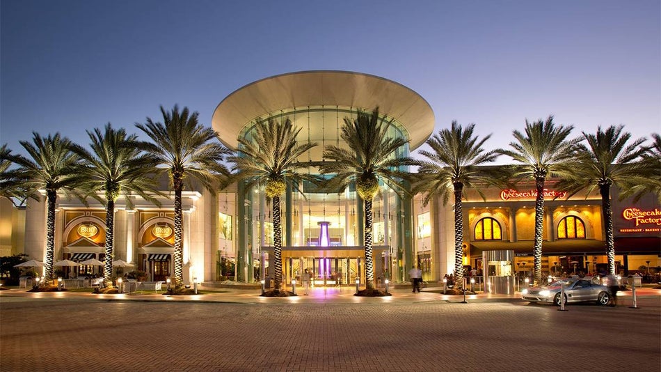 Wide shot of the front of the Mall at Millenia at dusk with their lights on and palm trees lining the front in Orlando, Florida, USA