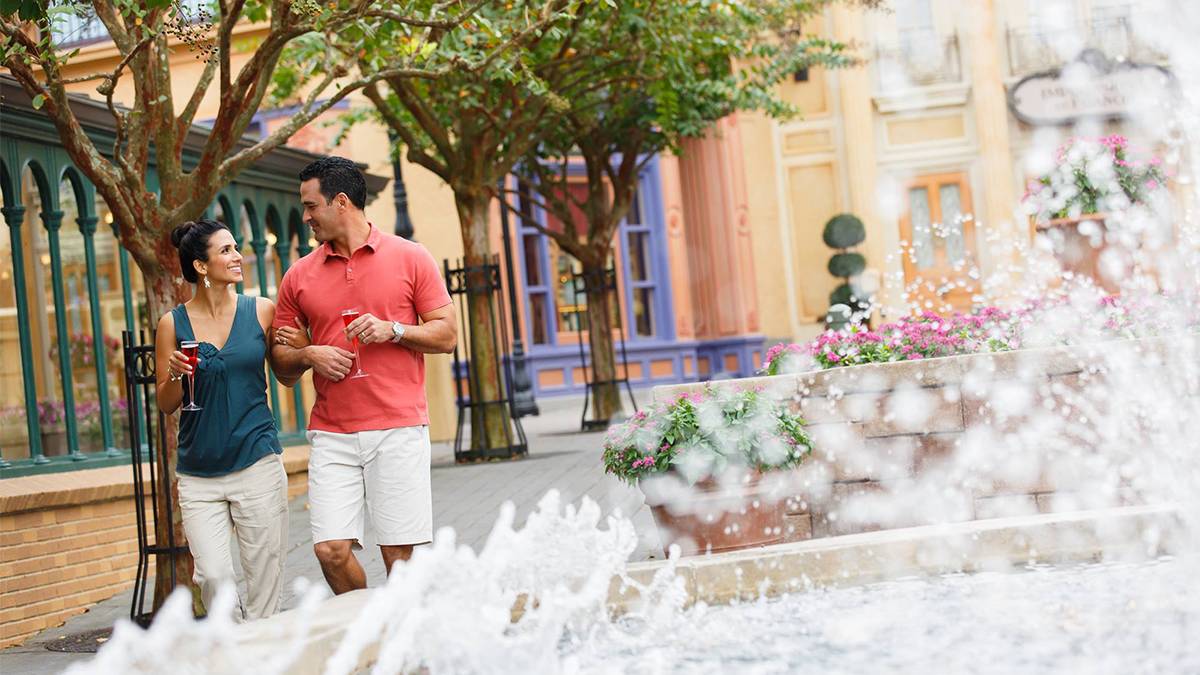 Man and Women with glasses of alcohol walking by a fountain in Walt Disney World in Orlando, Florida, USA