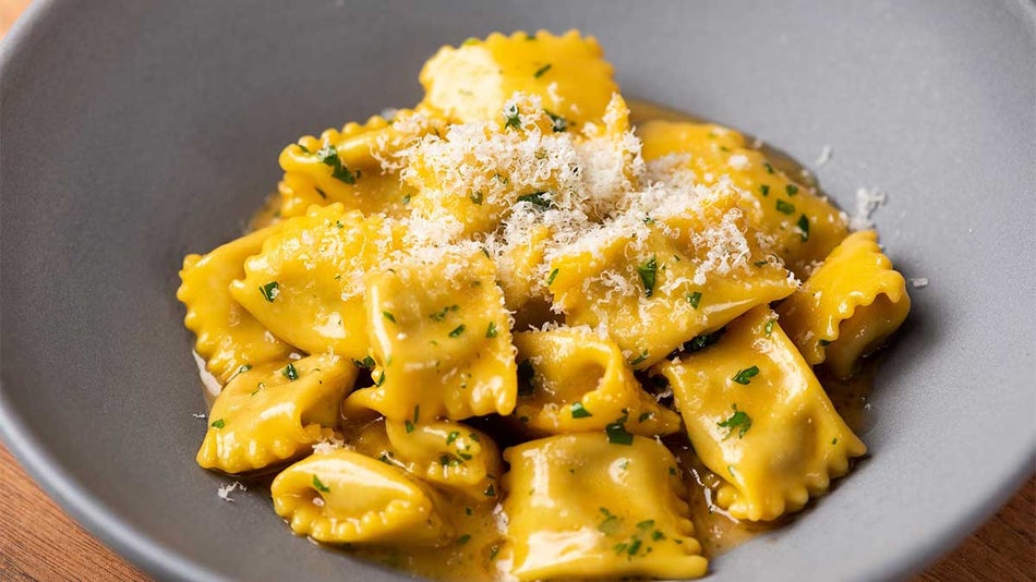 A small pile of ravioli pasta with a creamy muted yellow sauce on a matte grey plate from Penny Roma in San Francisco, California, USA