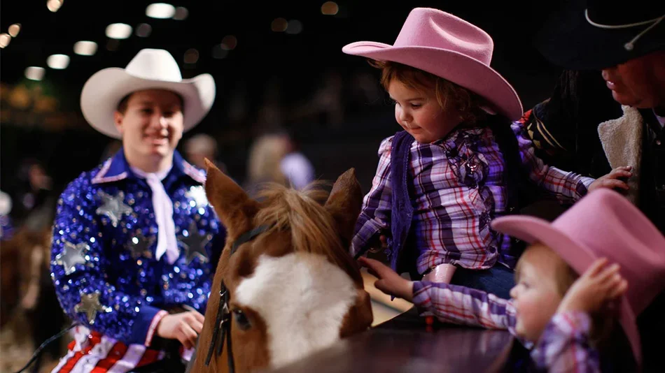 close up of toddlers in pink cowboy hats petting horse of performer at Dolly Parton’s Stampede in Pigeon Forge, Tennessee, USA