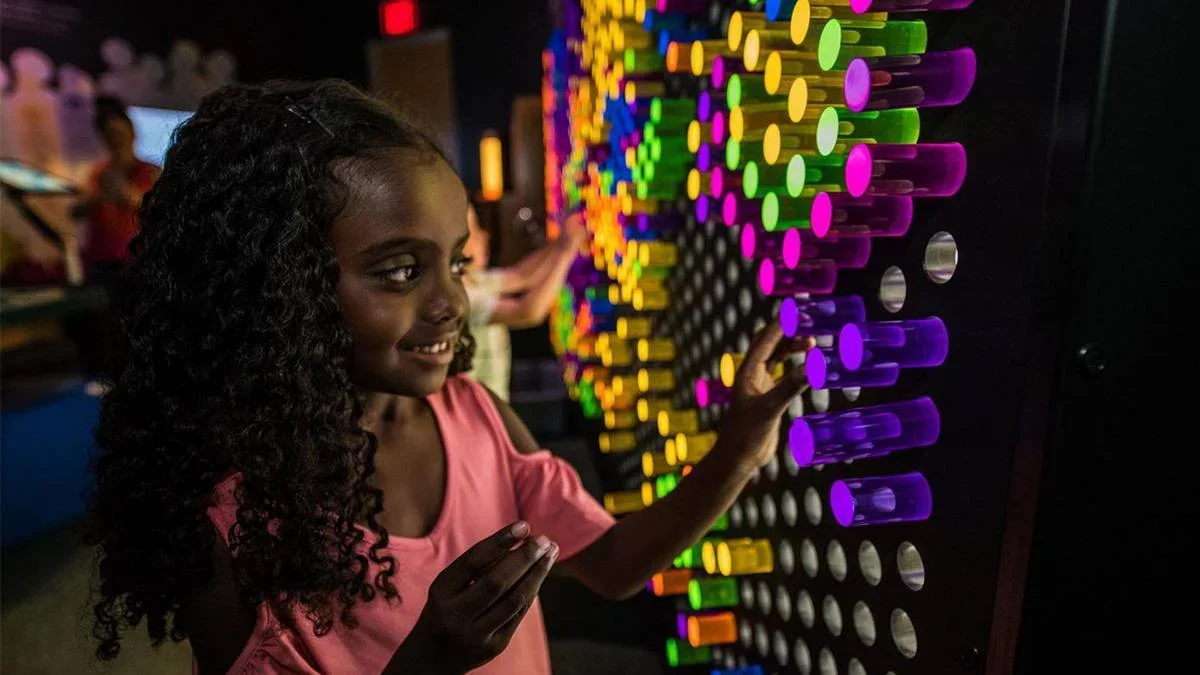 little girl playing with plug colored pegs in a Lite-Brite-style interactive mural in the DoSeum's Dream Tomorrow Today exhibition in San Antonio, Texas, USA