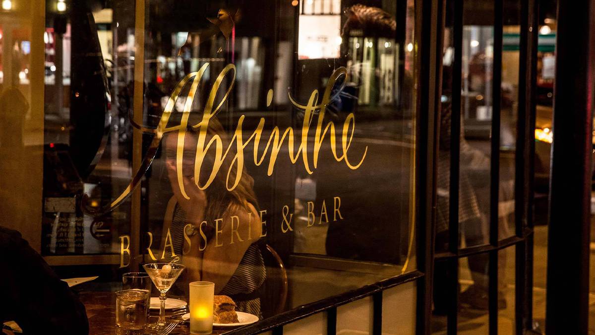 Close up shot of a window with Absinthe Brasserie & Bar printed on it in gold with people on the other side dining in San Francisco, California, USA