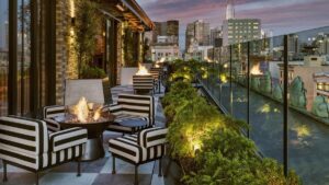 View of the outdoor lounge area with black and white stripped chairs with fire pits in the middle and plants lining the outer edge at Charmaine’s Rooftop Bar & Lounge in San Francisco, California, USA