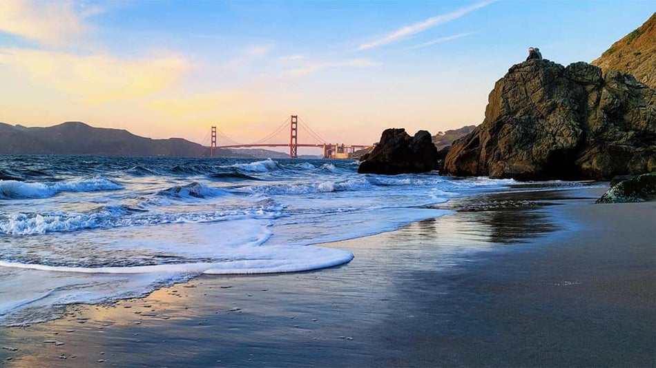 Looking over the beach with rocks on the right side and the Golden Gate Bridge in the background on China Beach at sunset in San Francisco, California, USA