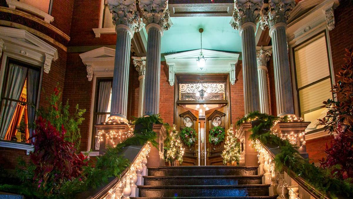 Front entrance to the Kehoe House at night with Christmas lights and garland wrapped around the stair railings