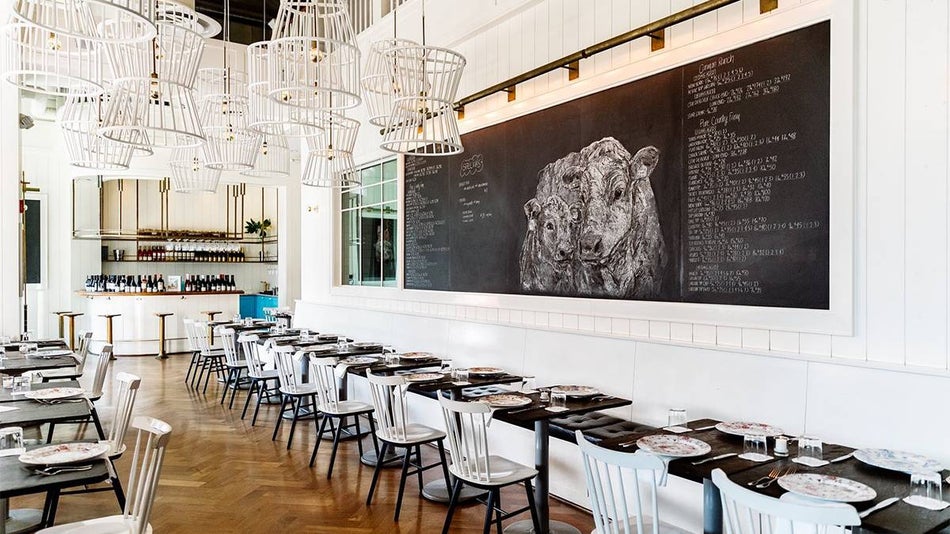 Dining tables pushed up against a white wall with a chalk board that has cows drawn on it at Bateau in Seattle, Washington, USA