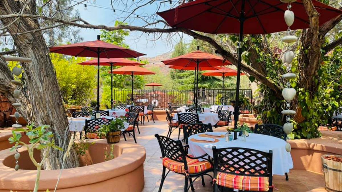 Wide shot of the outdoor dining area at Casa Sedona Restaurant, tables with white cloths and large red umbrellas covering them with lots of trees surrounding the dining area in Sedona, Arizona, USA