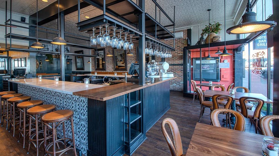 A bar with marble and wood counter tops and wine glasses hanging upside down from a shelf plus wooden stools and tables next to large windows at The Clinkscale in Sedona, Arizona, USA
