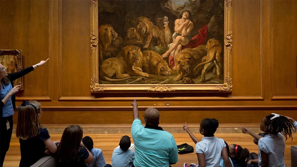 Wide shot of adults and children looking at a painting of a man and lions at the National Gallery of Art in Washington DC
