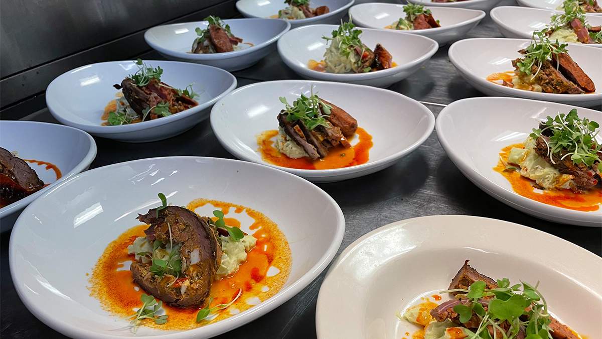 A stainless steel counter filled with white plates that have a steak dish with an orange sauce on it from Giuseppe's Italian Restaurant in Williamsburg, Virginia, USA