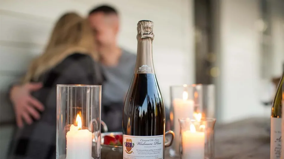 Close up photo of a bottle of wine with lit candles next to it and a couple kissing in the background at Williamsburg Winery in Williamsburg, Virginia, USA
