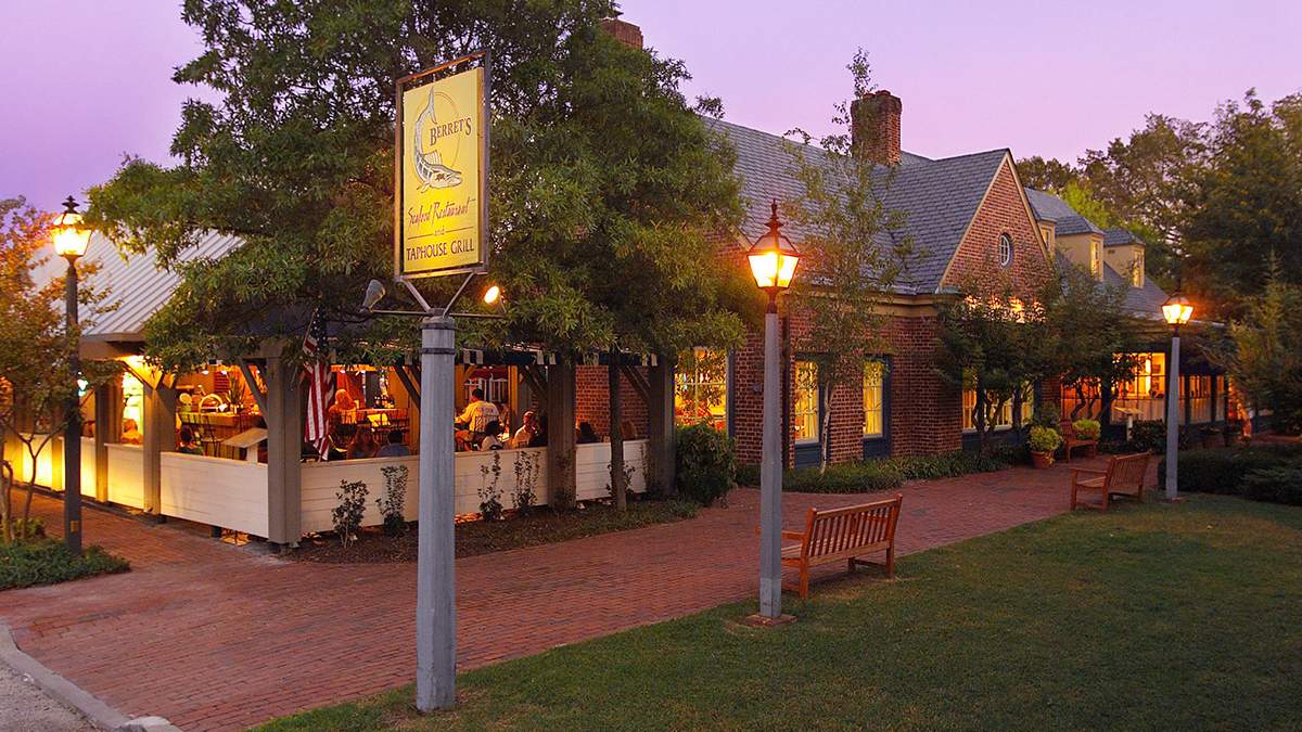A wide shot of the exterior of Berret's Seafood Restaurant & Taphouse Grill, a brick building with an outdoor seating area on the left side and a brick sidewalk leading up to it in Williamsburg, Virginia, USA