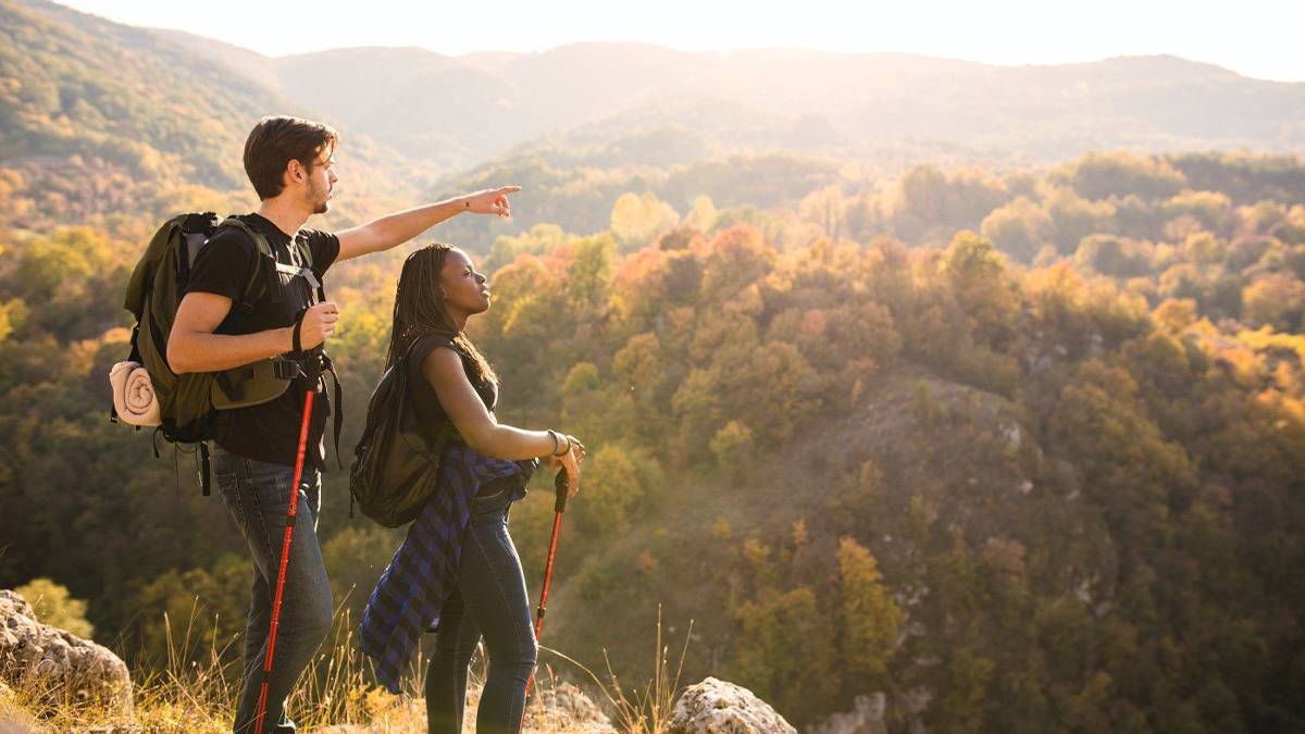 man and woman with walking hiking poles on trail overlooking mountains