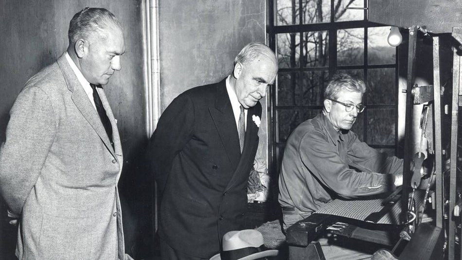Black and white photo of three men inspecting a weaving machine at Biltmore Industries Homespun Museum in Asheville, North Carolina, USA