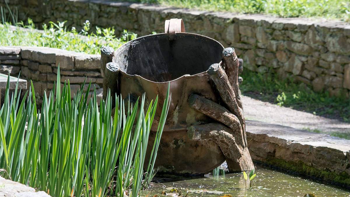 Statue in water of hands holding a bucket with tall grass next to it at the Botanical Gardens in Asheville, North Carolina, USA