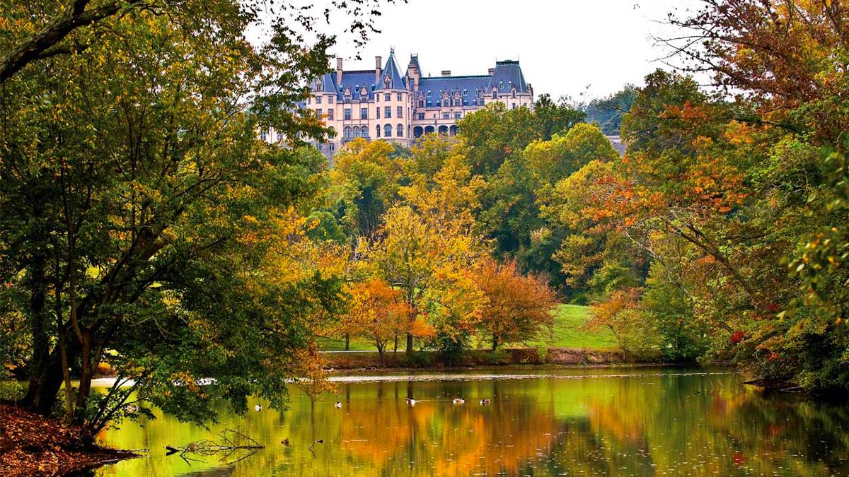 view of Biltmore Estate in background with autumn fall trees and lake in the front in Asheville, Tennessee, USA