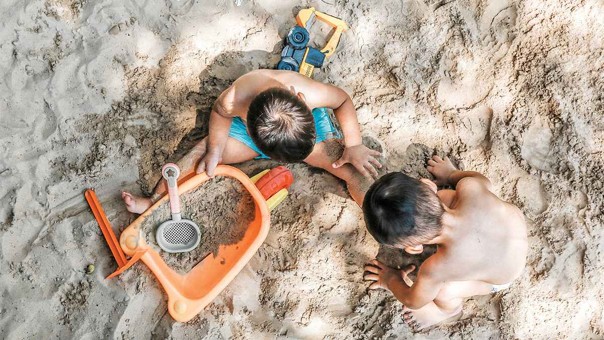 two kids toddlers playing in the sand on a sunny day