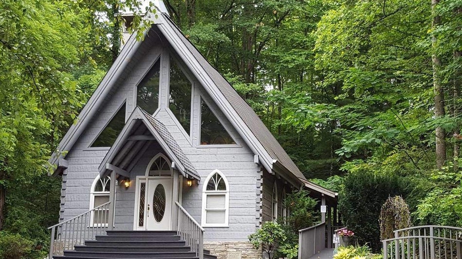 Exterior view of grey a-frame chapel surrounded by green trees in the smoky mountains