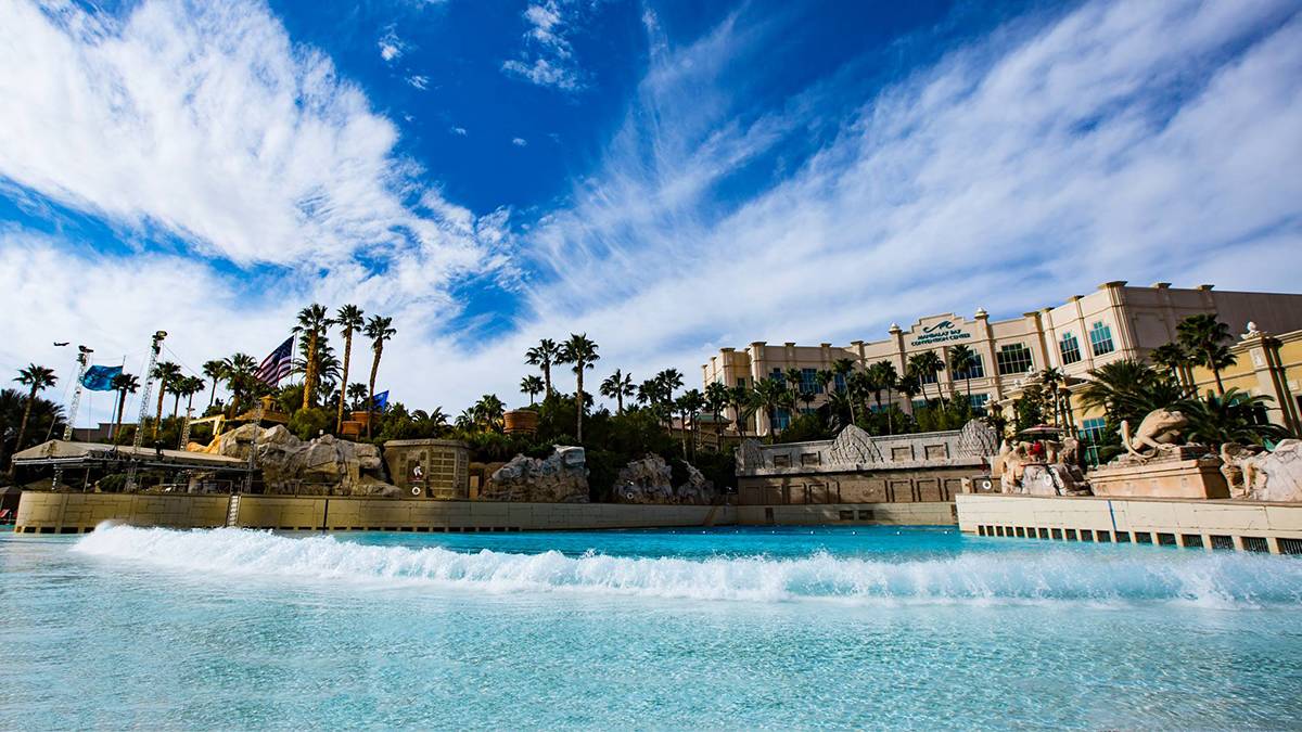 View of Mandalay Bay Resort and Casino from the wave pool with lots of palm trees and rocky decoration on a sunny day in Las Vegas, Nevada, USA