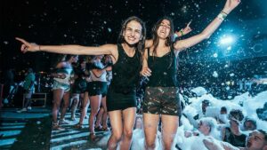 Close up photo of two girls having run a pool party with lots of people covered in bubbles in the pool behind them in Las Vegas, Nevada
