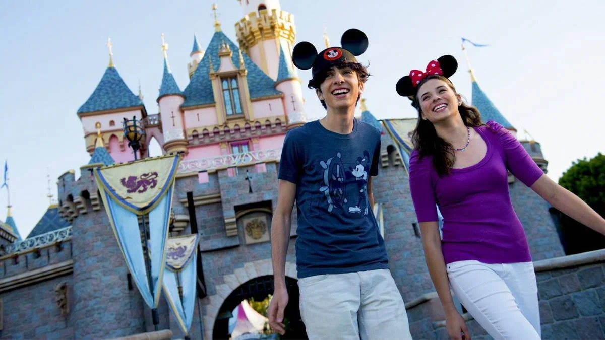 two people with mickey hats walking in front of disney castle in disneyland