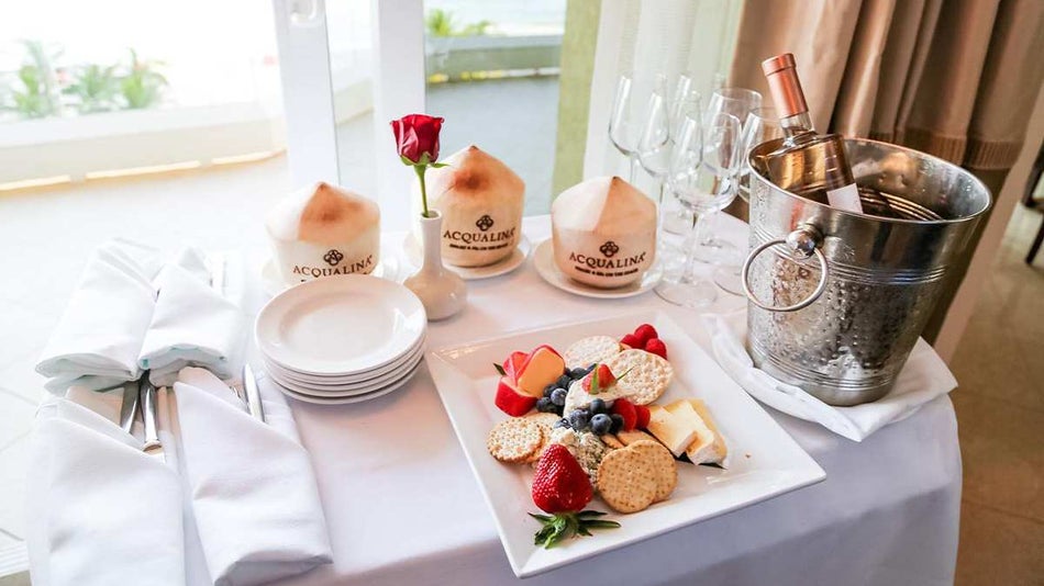 Table covered in a white cloth with a fruit and cheese board on it and three skinned coconuts with the Acqualina Resort & Spa logo burned into them and a bottle of alcohol on ice at the Acqualina Resort & Spa in Miami, Florida, USA