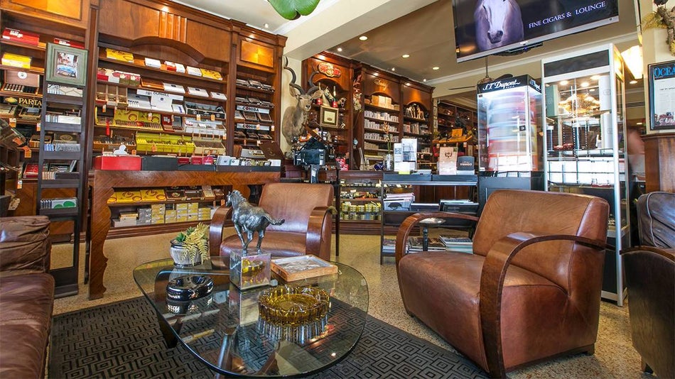 Wide shot of the interior of the Little Havana Cigar Factory with boxes of cigars on the walls and leather chairs around a glass table in Miami, Florida, USA