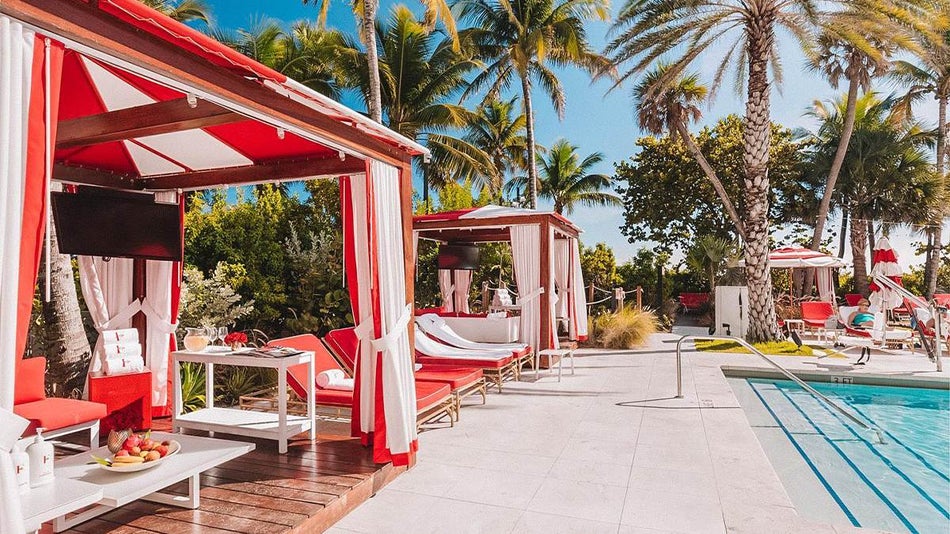 Several red and white beach cabanas stocked with fruit and other amenities pool side at Faena Hotel Miami Beach in Miami, Florida, USA