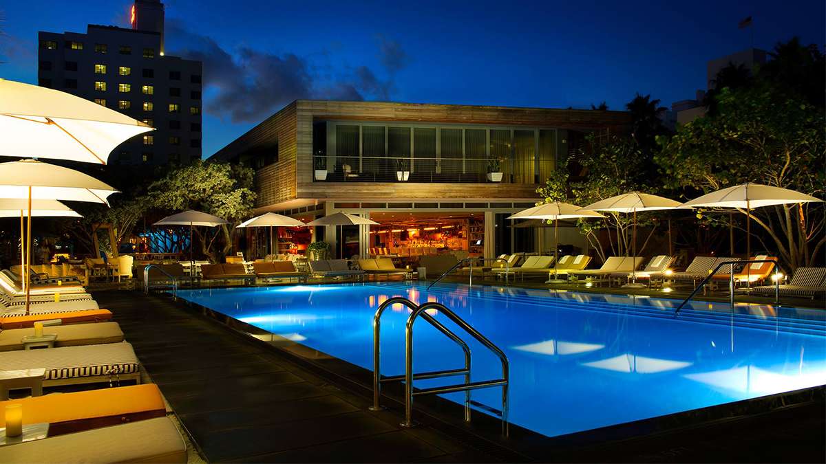 Wide shot of the outdoor pool at night surrounded by lounge chairs with the hotel in the background at Hyde Beach in Miami, Florida, USA