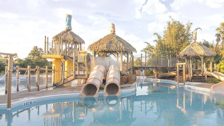 Three tiki huts with water slides coming out of them into a light blue pool at Liki Tiki Village in Miami, Florida, USA