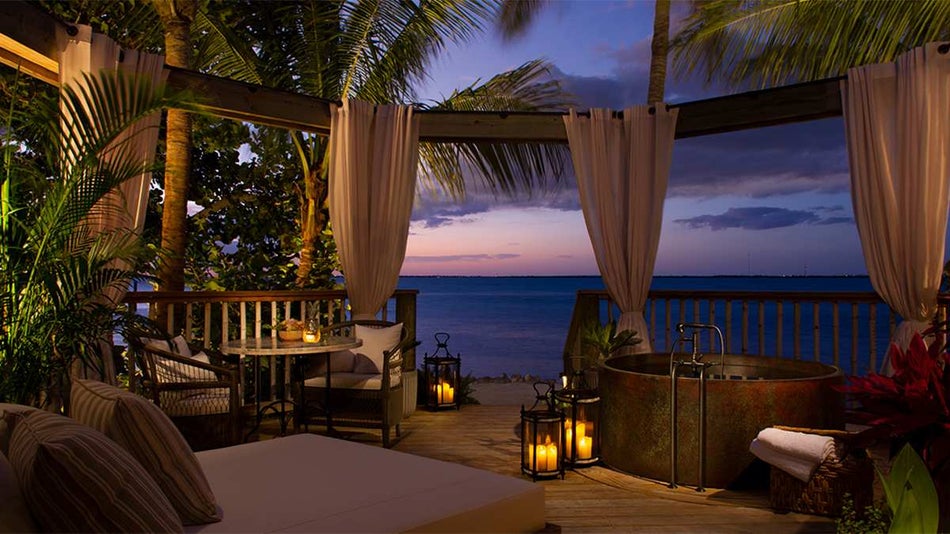 A private beach side area with a bed, bathtub, and dining area along the beach at sunset at Little Palm Island Resort & Spa in Miami, Florida, USA