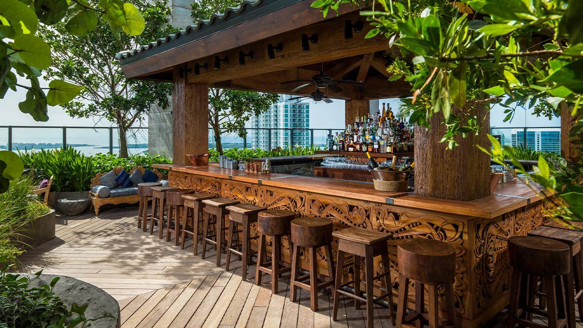 View of the wooden bar with designs carved in it and wooden tools of different shape plus greenery surrounding it and the city in the background at Sugar Rooftop Bar in Miami, Florida, USA