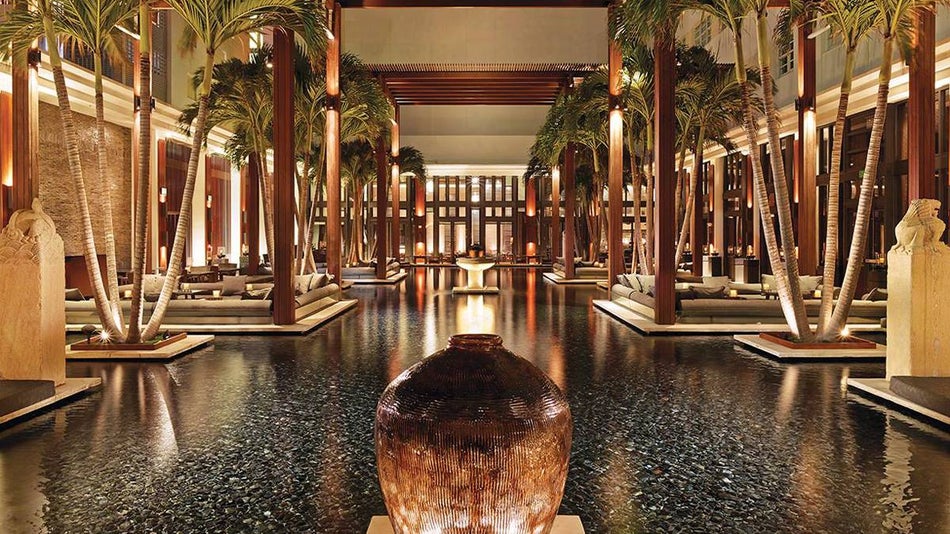 An indoor swimming pool with palm trees, low light, and wooden accents at The Setai Miami in Miami, Florida, USA