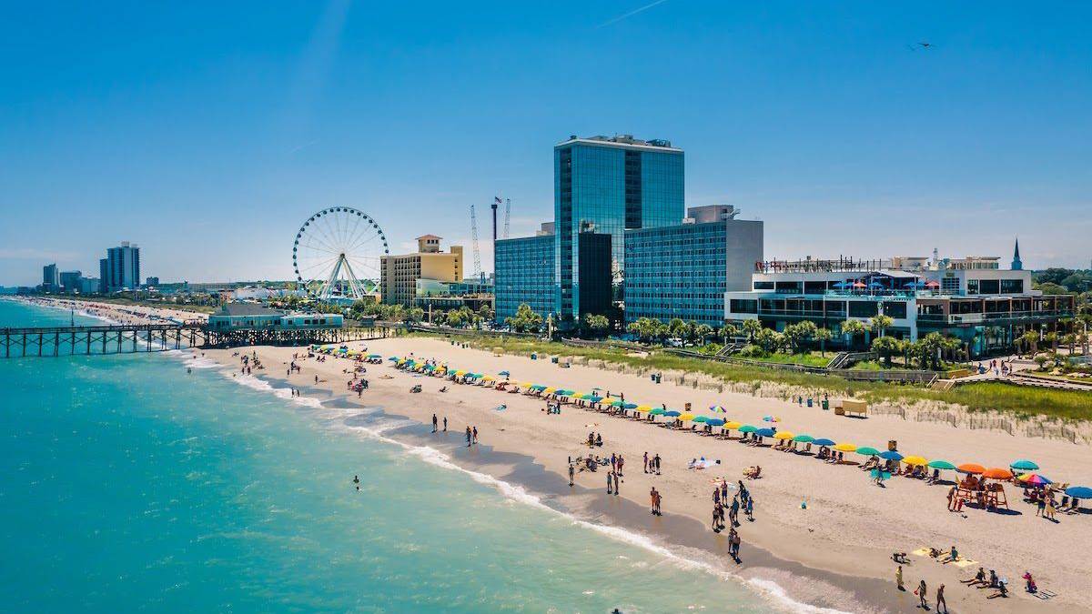 People at Myrtle Beach by the shore with buildings and a Ferris wheel in the background.