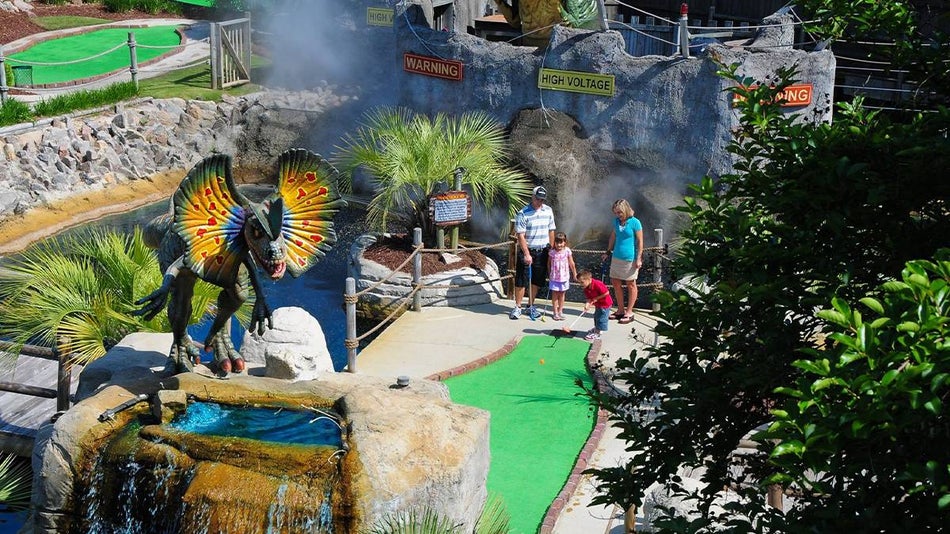 View looking down on a family playing mini golf on a sunny day with a dinosaur on top of a rock at Jurassic Park Mini-Golf in Myrtle Beach, South Carolina, USA