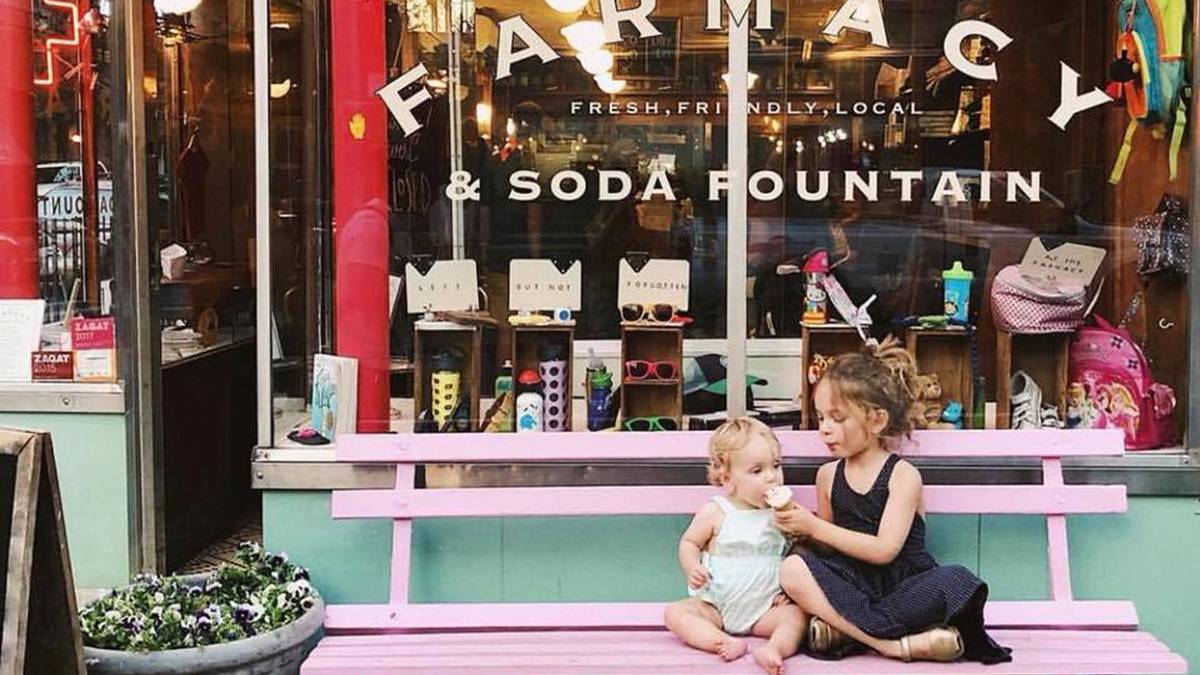 two children sitting on a pink bench eating ice cream outside of Brooklyn Farmacy and Soda Fountain in NYC, New York, USA