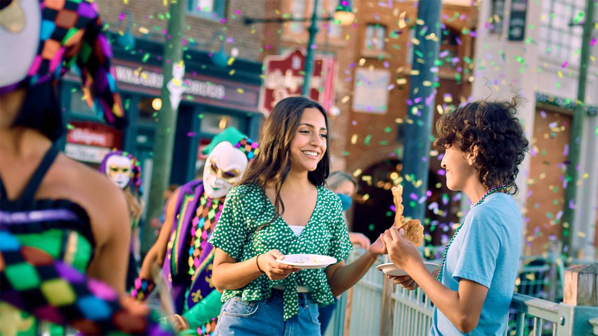 Couple eating during the Mardi Gras parade with confetti falling and people in costume next to them at Universal Orlando Resort in Orlando, Florida, USA