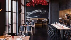 Dark walled dining area with a red flower chandelier and floor to ceiling windows on one wall at CAPA