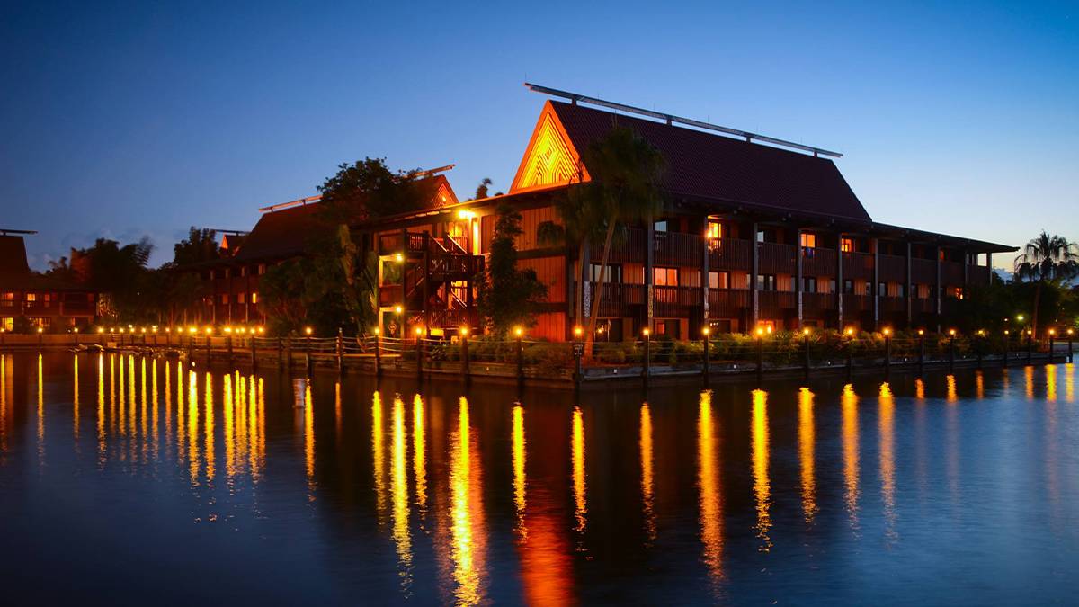 Wide shot of the Polynesian Village Resort at night with their lights on and the golden reflection of the lights in the water in Orlando, Florida, USA