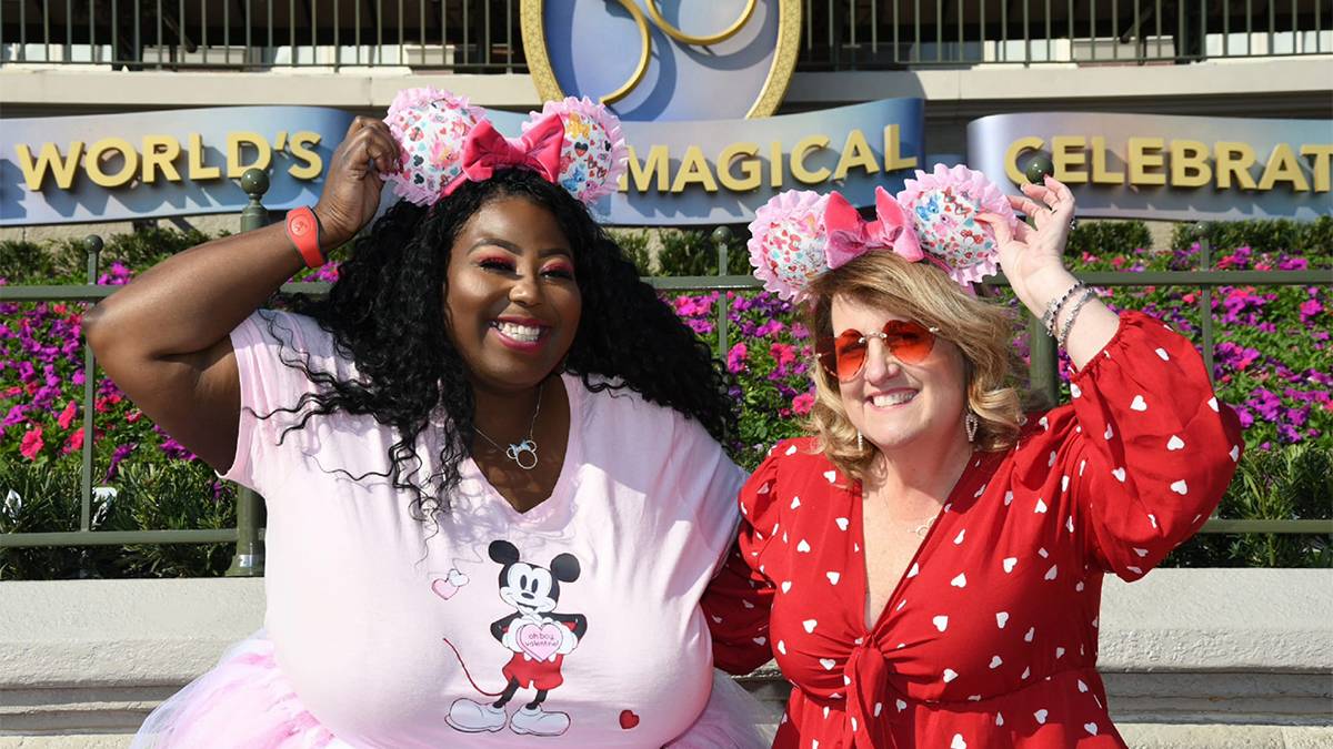 Two women in bright pink and red outfits showing off their matching pin ears and bows at Walt Disney World in Orlando, Florida, USA