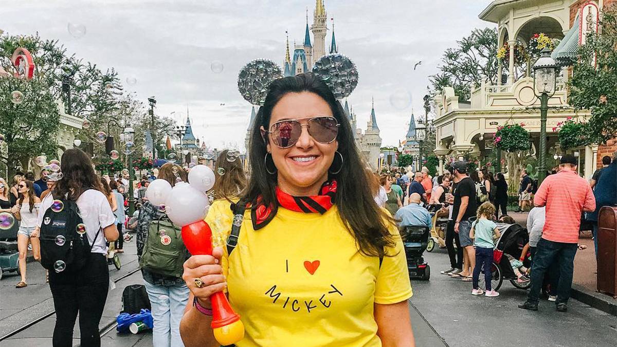 Close up of a women in a yellow shirt with ears and sunglasses on holding a bubble wand in front of the castle as Walt Disney World in Orlando, Florida, USA