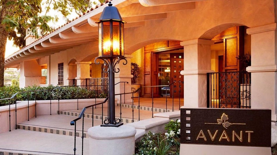 Exterior view of entrance to AVANT restaurant, a cream colored stucco building with black gaslamp and avant sign